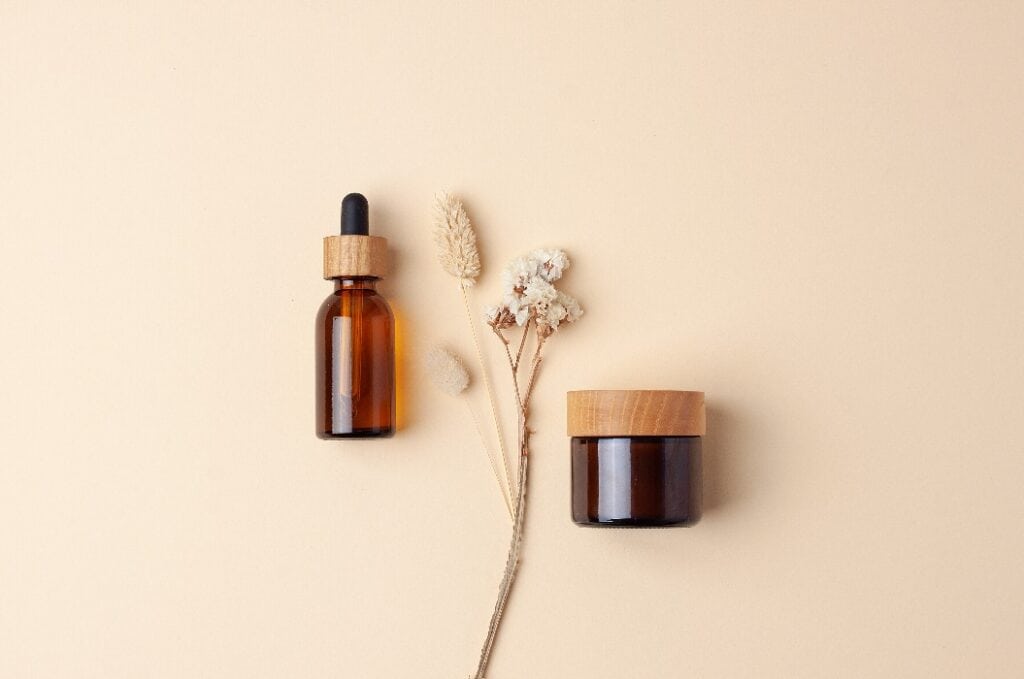 Minimal composition with cosmetic skin care products and flowers on pastel beige background. Flat lay.