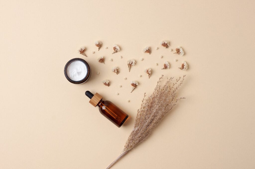 Minimal composition with cosmetic skin care products and flowers on pastel beige background. Flat lay, copy space